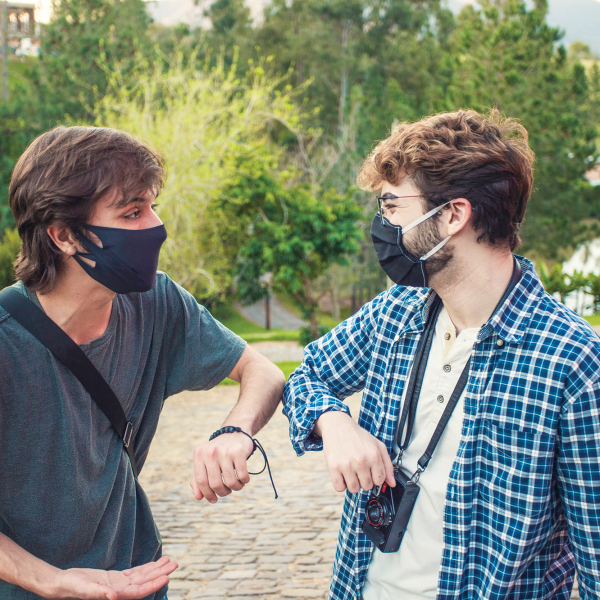 Two young men with masks bump elbows to greet each other in a park